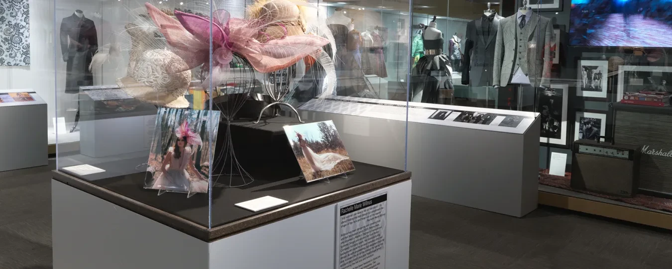 Museum exhibit with colorful sculpture in glass case, surrounded by photographs and displays on modern clothing.