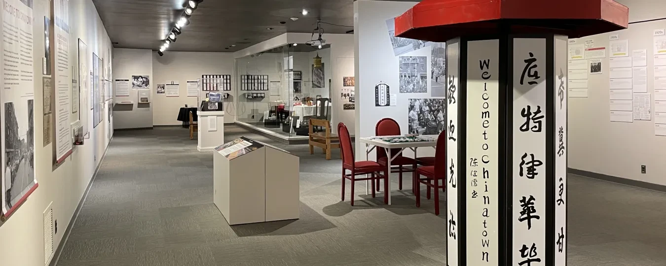 Museum exhibit with historical photographs and displays, featuring a lantern-like column with red roof and Chinese characters.