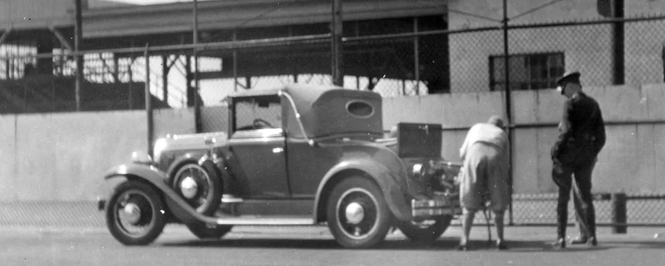 Vintage car parked for inspection with a woman opening the trunk. 