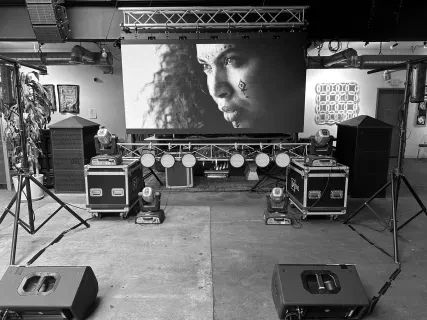 Concert stage setup with speakers, lights, and a large screen showing a woman's face in black and white.