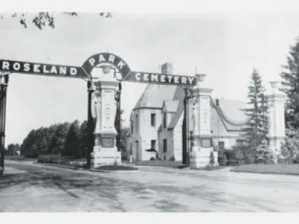 Grayscale photo of Roseland Park Cemetery entrance with arch and large trees nearby.