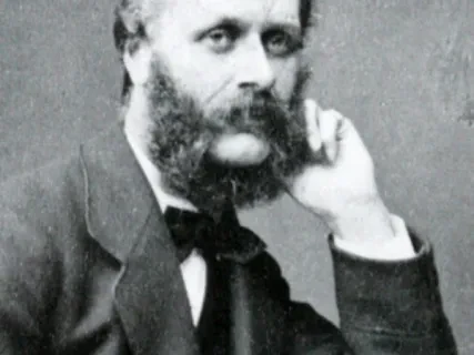 Bearded man in a suit, resting his head on his hand, gazing thoughtfully. Black and white photograph.