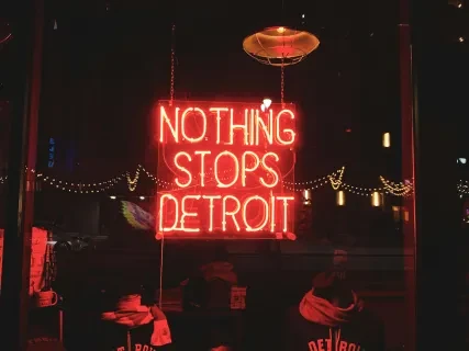 Red neon sign reads "Nothing Stops Detroit" above jackets and hats.