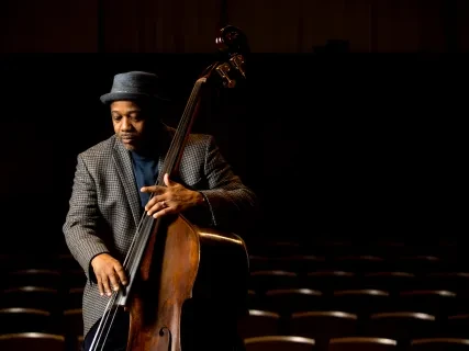 Man in a hat playing an upright bass on a dimly lit stage.