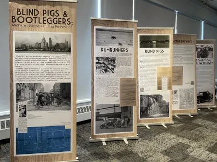 Exhibition banners display historical content on blind pigs and bootleggers in a room with carpeted floor and natural lighting.