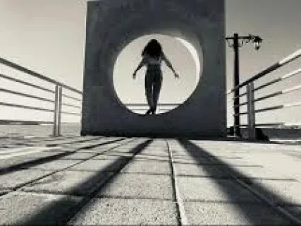 Silhouette of a woman inside a large circular sculpture on a boardwalk, with shadows and railings visible. Black and white photo.