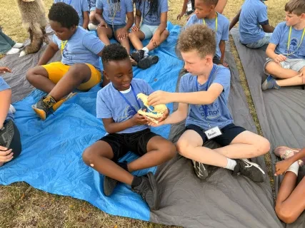Children sitting on a tarp outdoors, engaged in a playful activity with colored clay.