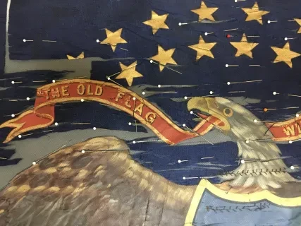 Eagle holding a red banner in its beak against a blue background with stars.
