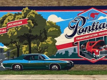 Colorful mural of classic cars with trees and "Pontiac, Michigan" signage on a brick wall.
