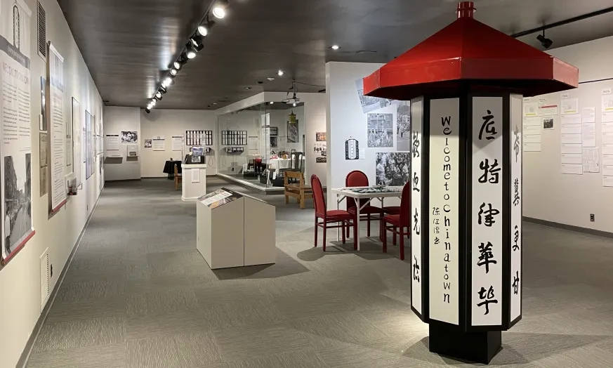 Museum exhibit with historical photographs and displays, featuring a lantern-like column with red roof and Chinese characters.