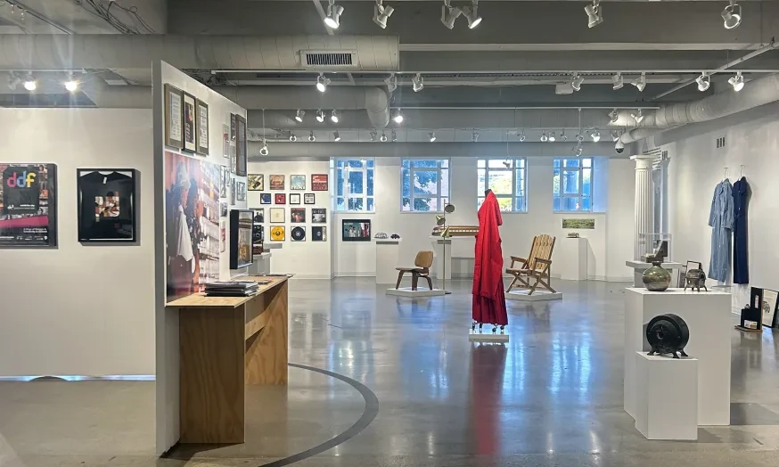 Spacious art gallery with various framed artworks on white walls, sculptures, and a bright red dress in the center.