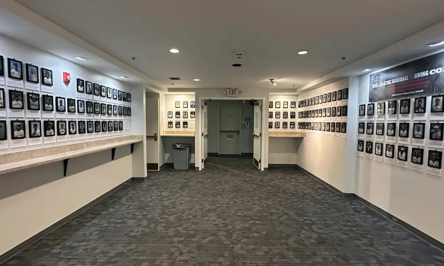 Hallway lined with framed photographs on both sides, gray carpet, and ceiling lights.