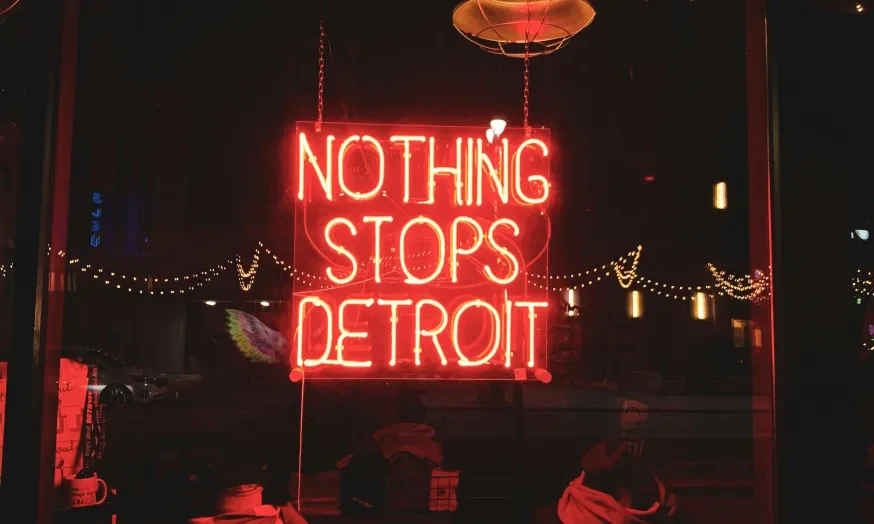 Red neon sign reads "Nothing Stops Detroit" above jackets and hats.
