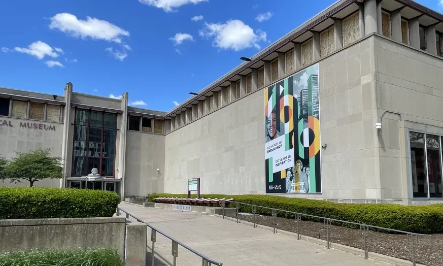 Museum exterior with modern architecture, a large colorful banner, and clear blue sky.