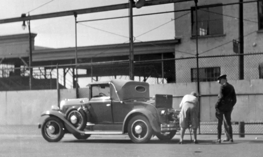 Vintage car parked for inspection with a woman opening the trunk. 