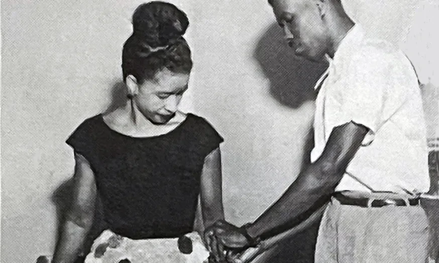 A man offers assistance to a woman wearing a polka dot skirt.