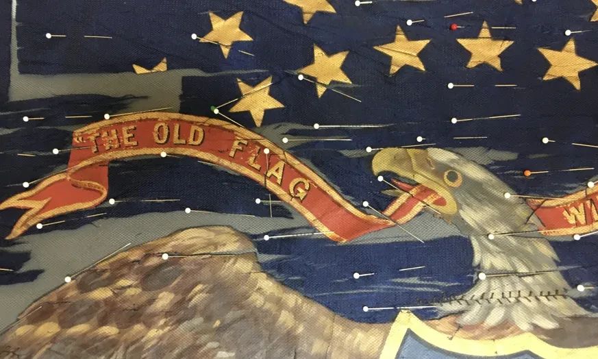 Eagle holding a red banner in its beak against a blue background with stars.