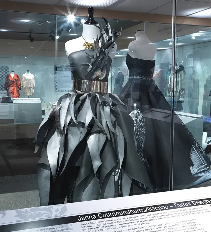 Futuristic black dresses on mannequins in a display case, featuring metallic textures and intricate designs.
