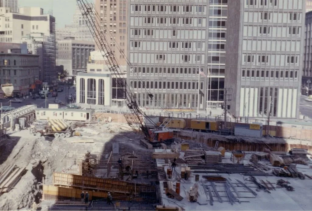 Construction site with cranes and machinery in a city, surrounded by tall buildings under a clear sky.