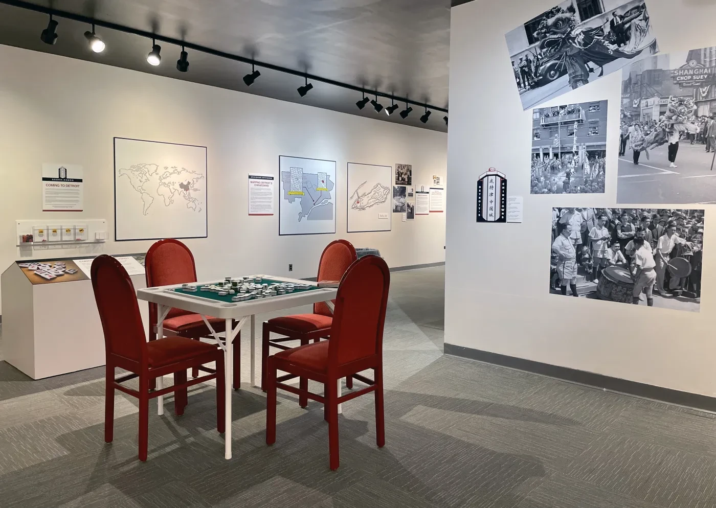 Gallery room with red chairs around a table; black-and-white photos displayed on white walls.