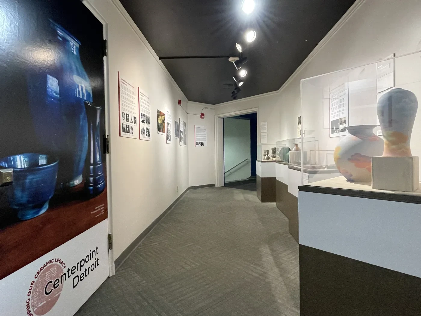 Hallway in an art gallery with pottery on display and framed artwork on the walls.