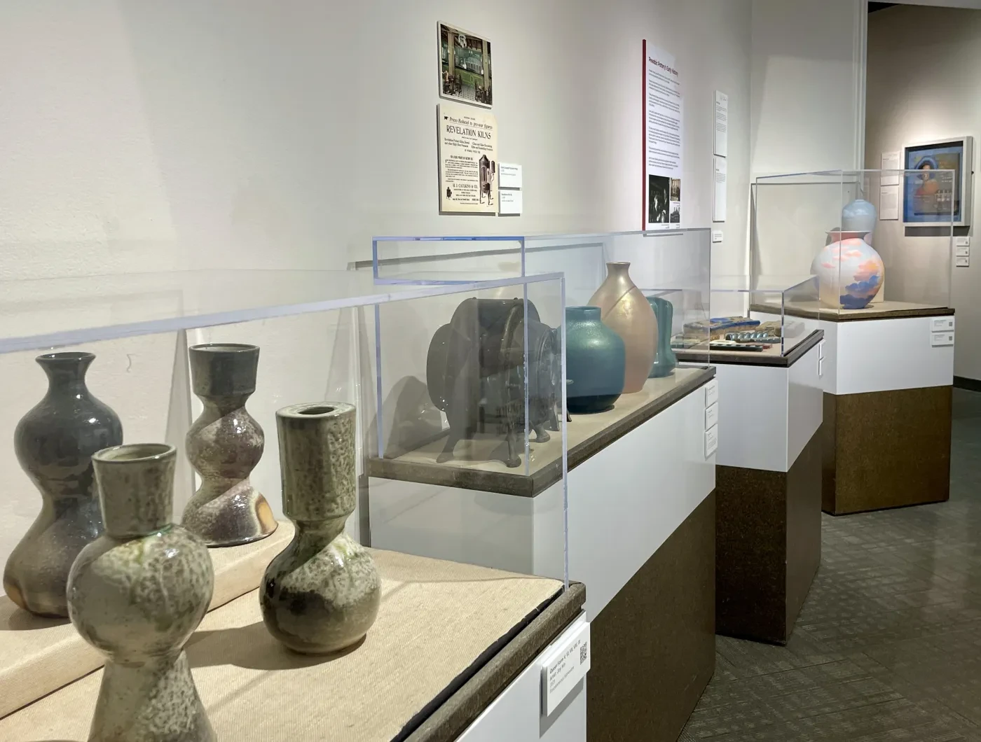 Vases displayed in a museum exhibit, with varying shapes and colors, under protective glass cases.