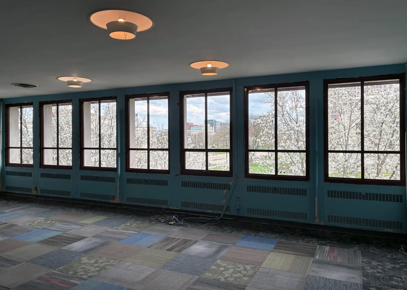 Spacious room with large windows and patterned carpet, overlooking blooming trees outside.