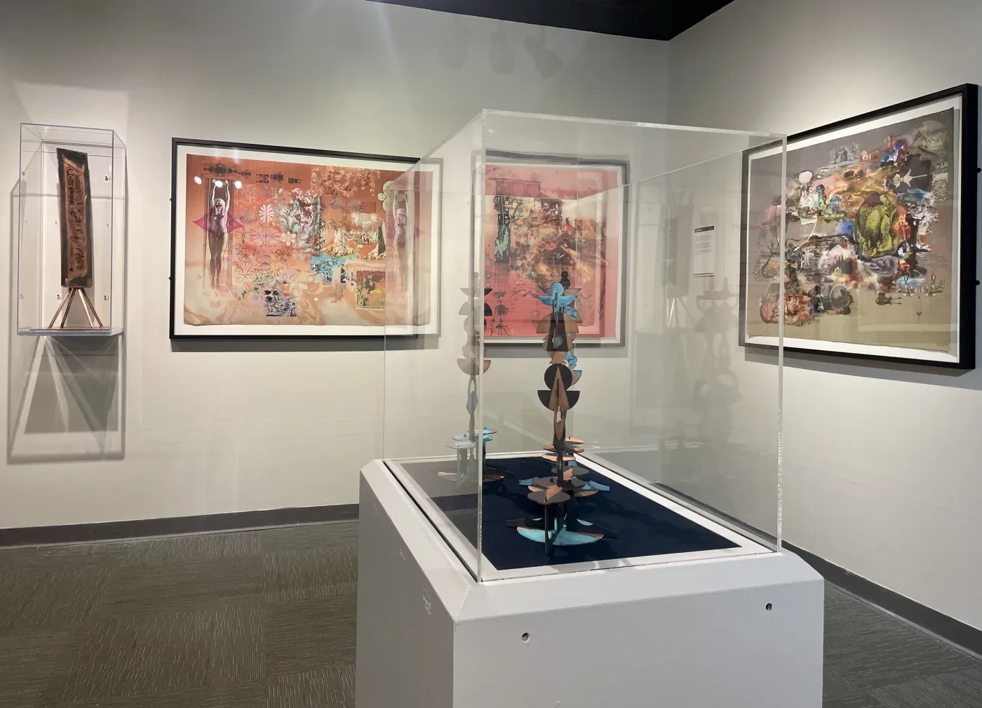 Art gallery with colorful paintings on walls and a sculpture in a glass case at the center.