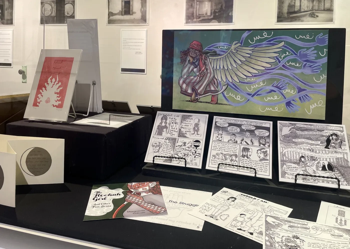 Exhibition display of colorful winged creature art and various black-and-white comic panels.