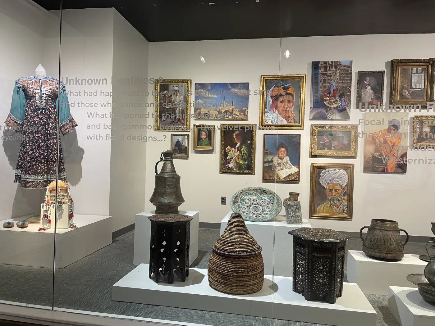 Museum exhibit with traditional clothes, pottery, and framed artwork on walls.