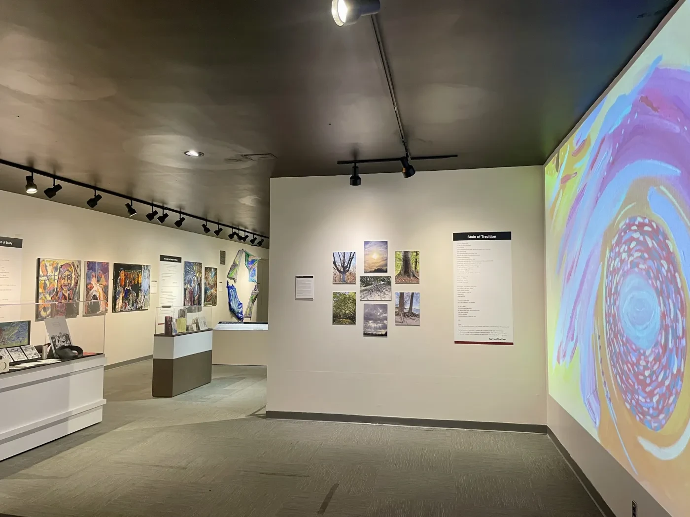 Art gallery interior with colorful paintings, a large abstract display on the right, and soft overhead lighting.