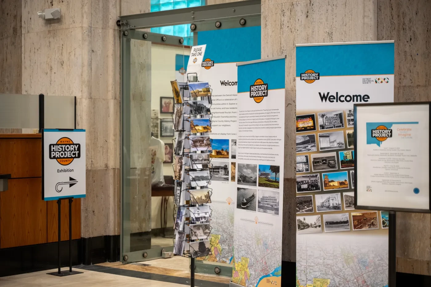 Colorful informational banners and a postcard rack in a lobby entrance, with a modern wooden and stone decor.