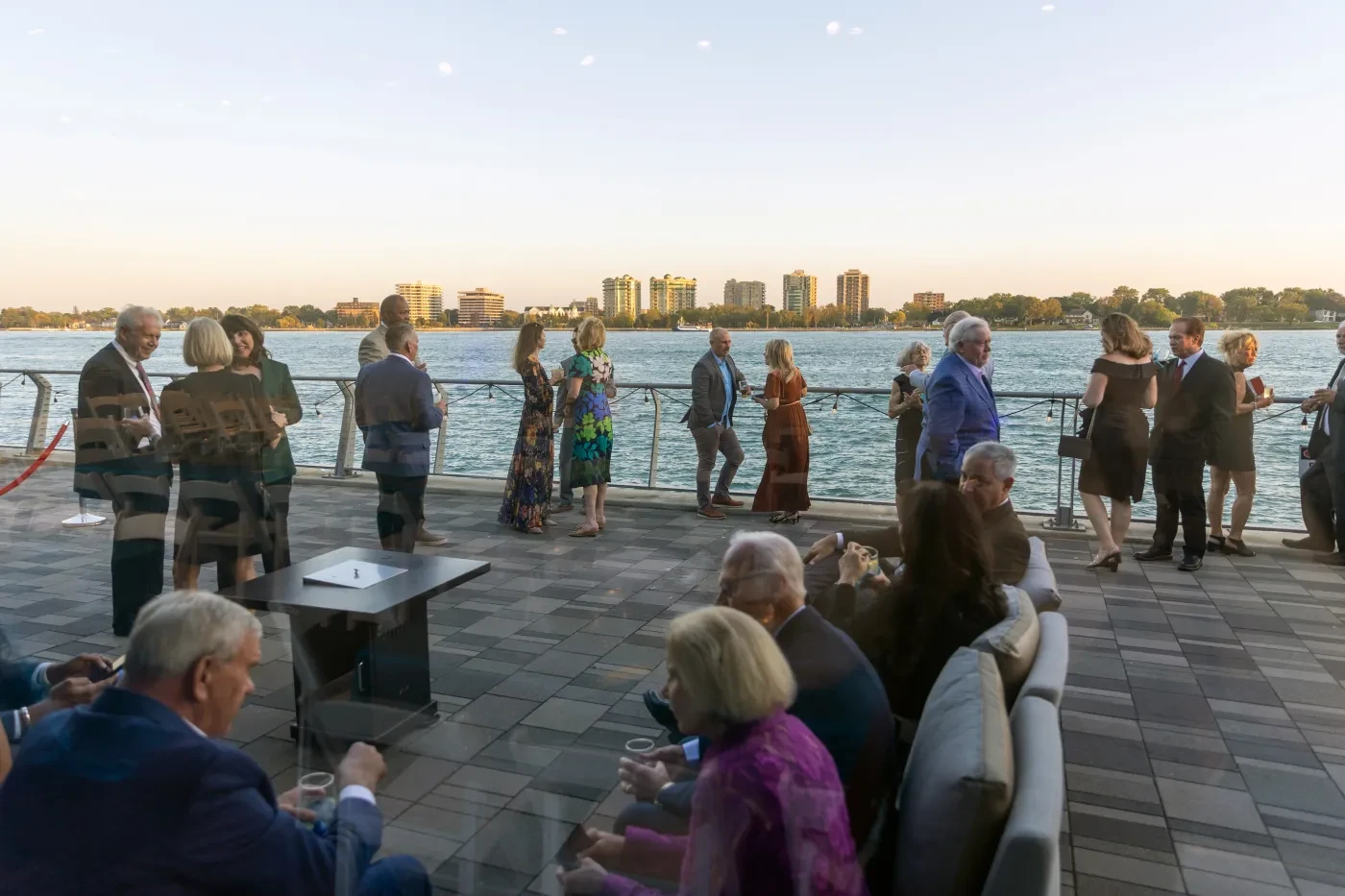 People gathered on a waterfront terrace at sunset, enjoying the view and socializing.
