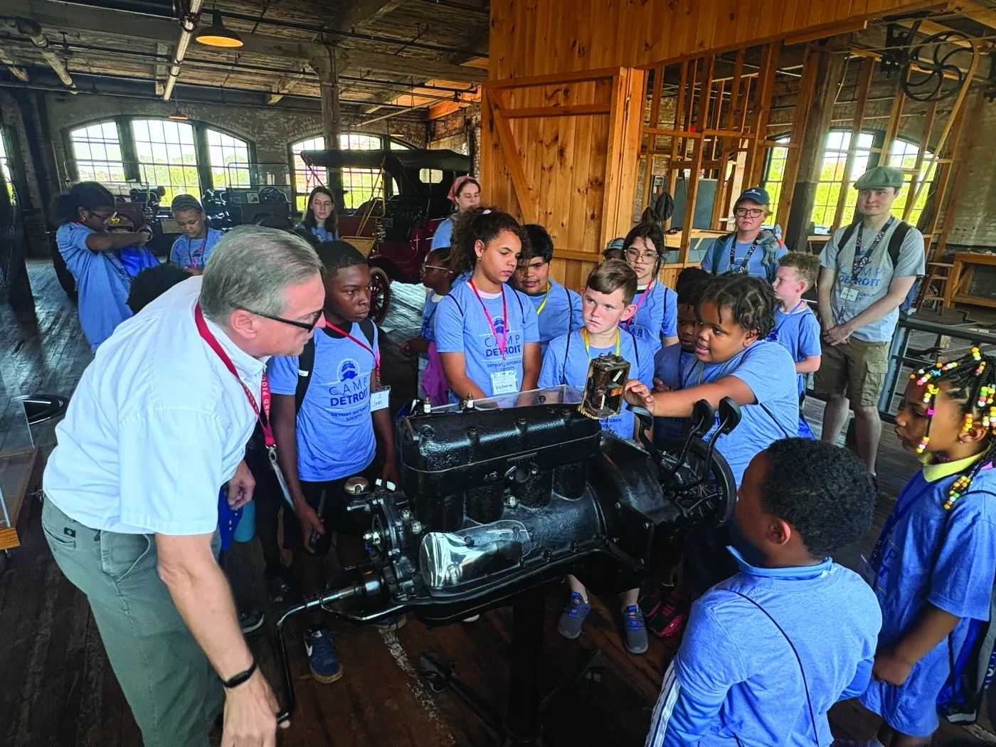Children gathered around an engine exhibit, guided by an instructor in a museum setting.