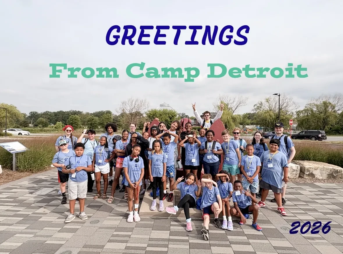 Group photo of kids and adults in matching blue shirts at an outdoor camp setting.
