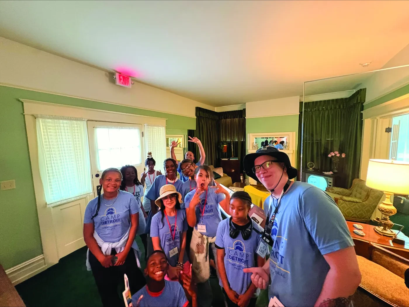 Group of people in matching blue shirts smiling in a cozy, well-lit room with green and white decor.