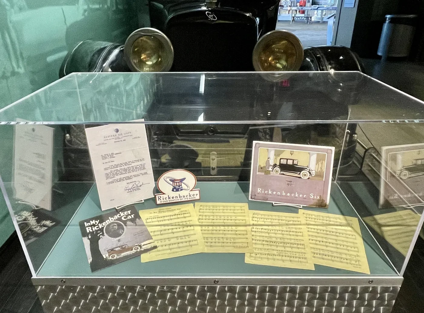 Display case with vintage car memorabilia, including documents and a photograph.