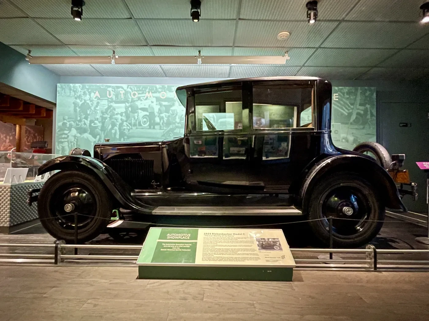 Black vintage car displayed in a museum exhibit with informational plaques.