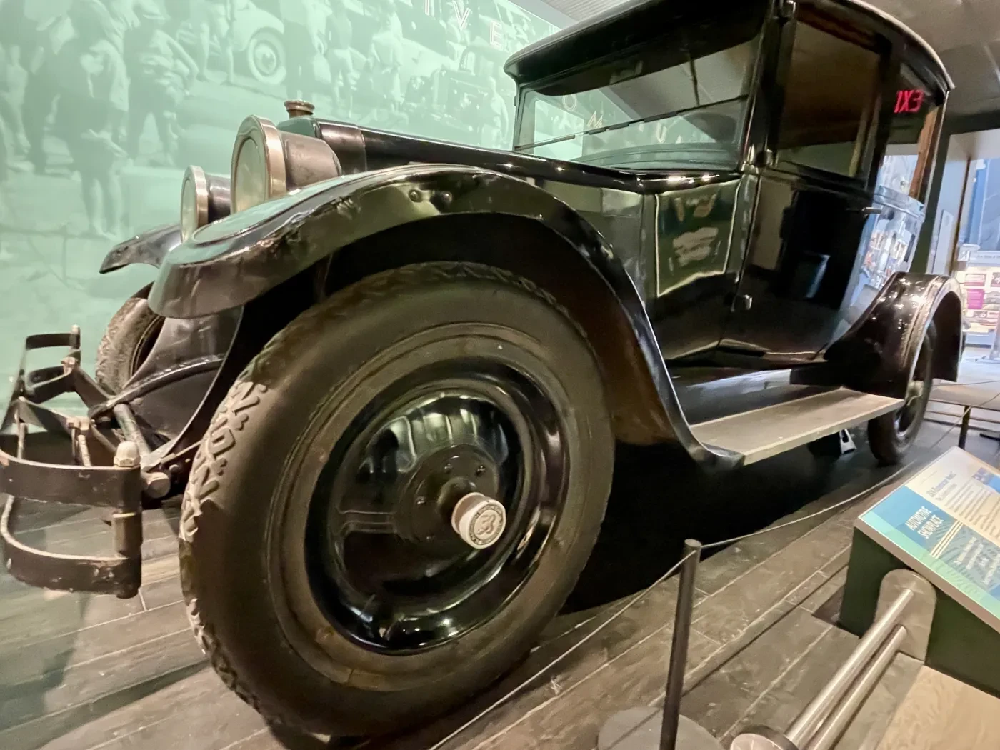 Antique black car displayed in a museum with informational signage and photographs in the background.