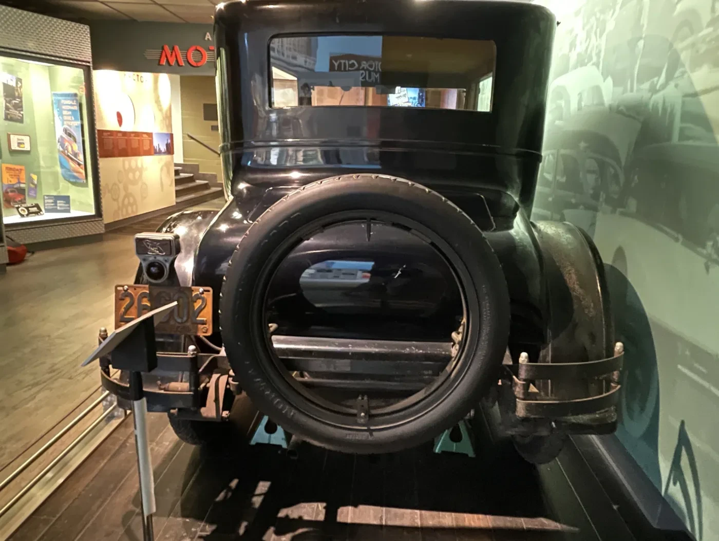 Black vintage car displayed in a museum, viewed from the rear, with a spare tire mounted at the back.