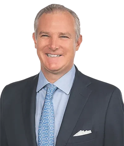 Smiling man in a suit with a blue patterned tie against a plain background.