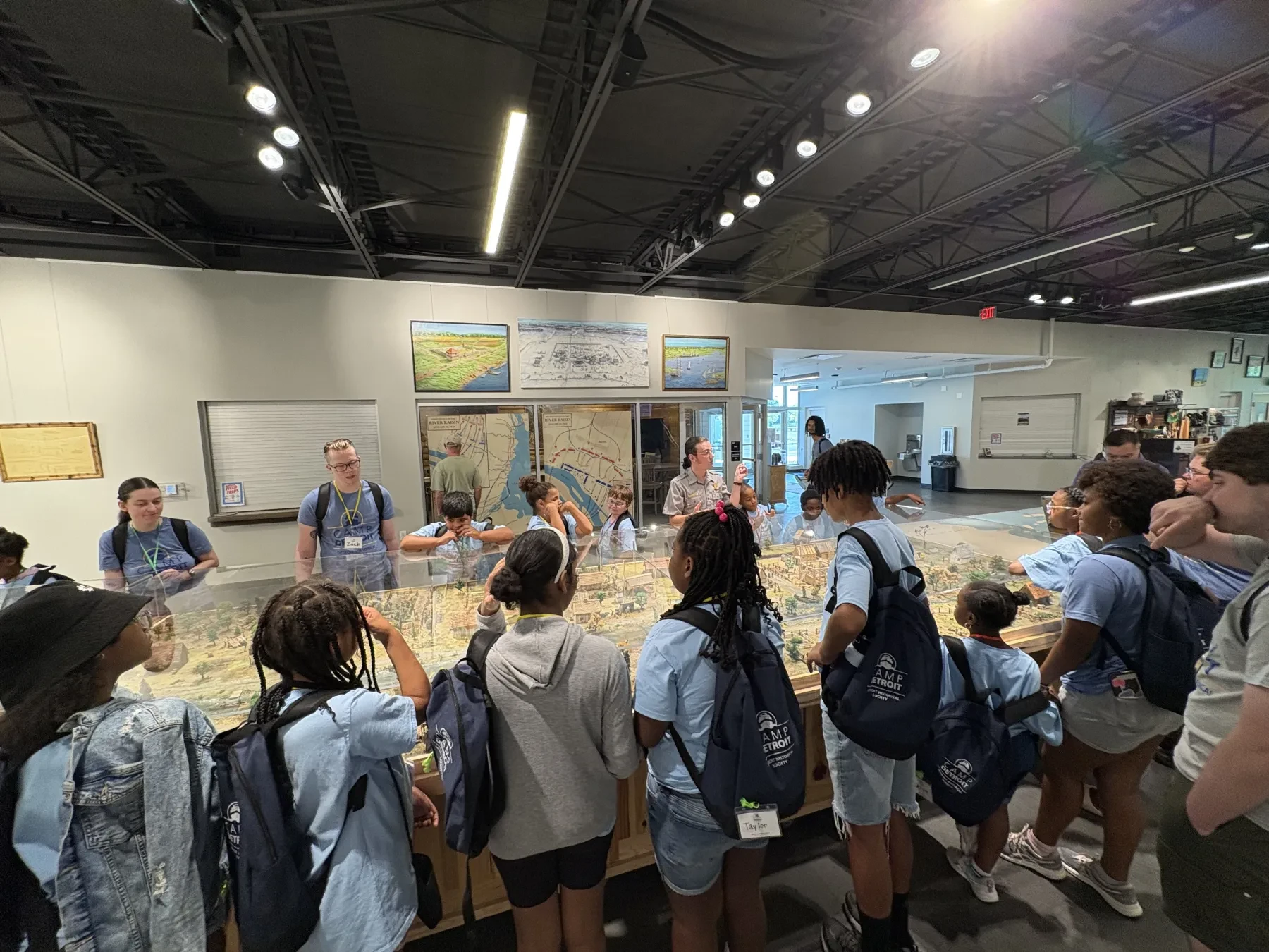 Group of students in blue uniforms observing a large table model in a museum exhibit hall.