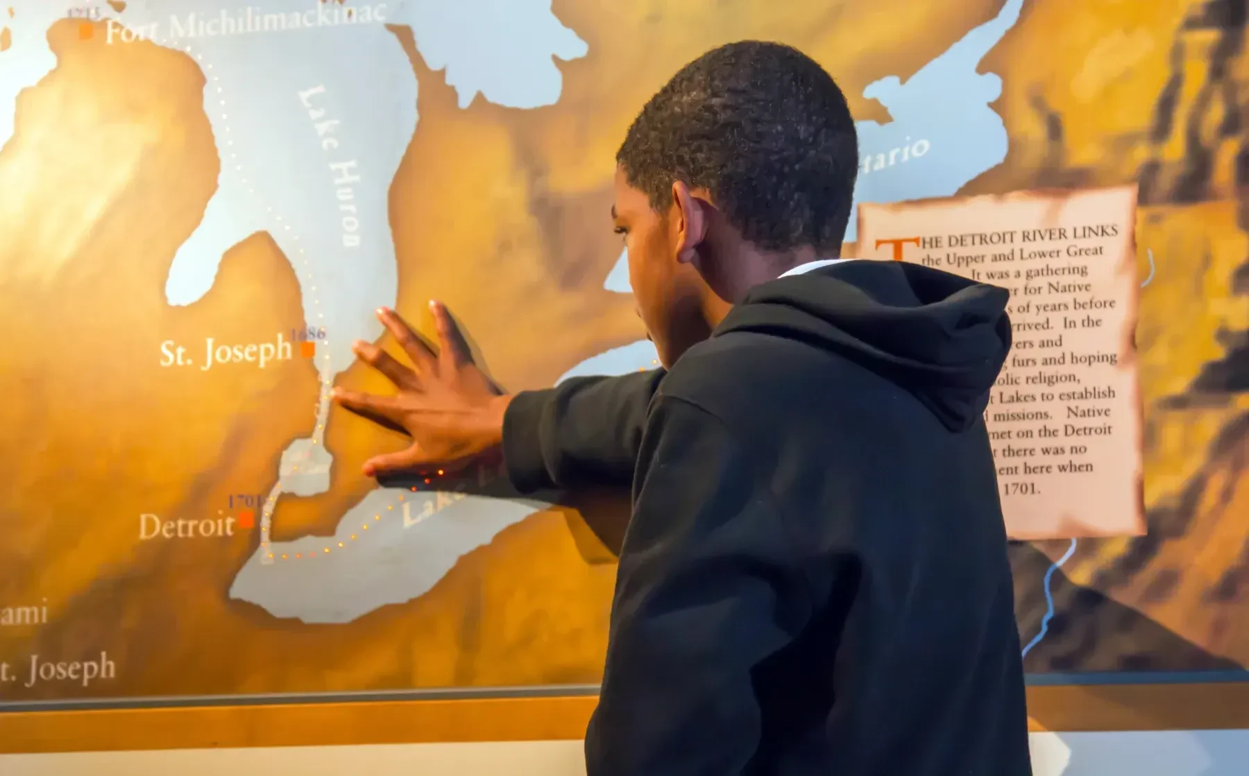 A person touches a large, colorful map on a museum wall, studying the area with focus.