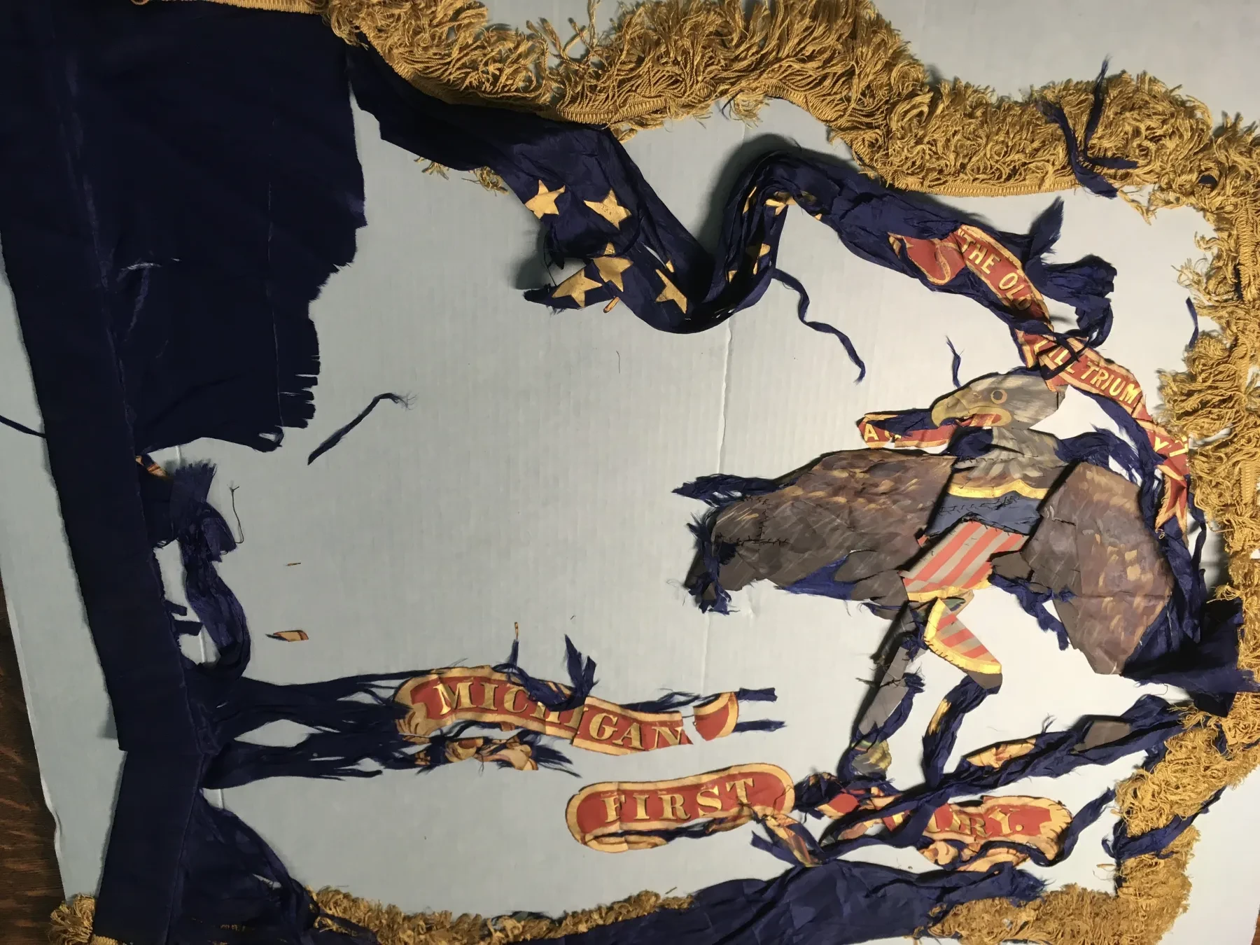 Tattered blue banner with gold fringe featuring a colorful eagle and star motifs.